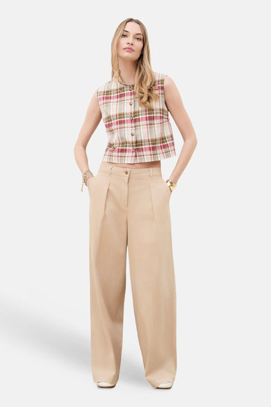 Chino beige de CAROLL, un pantalon taille haute à coupe large, porté avec un haut à carreaux et des bracelets dorés.