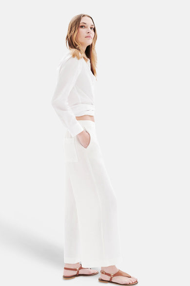 Pantalon blanc de CAROLL, ample, à poches latérales, porté avec une chemise blanche nouée et des sandales en cuir marron.