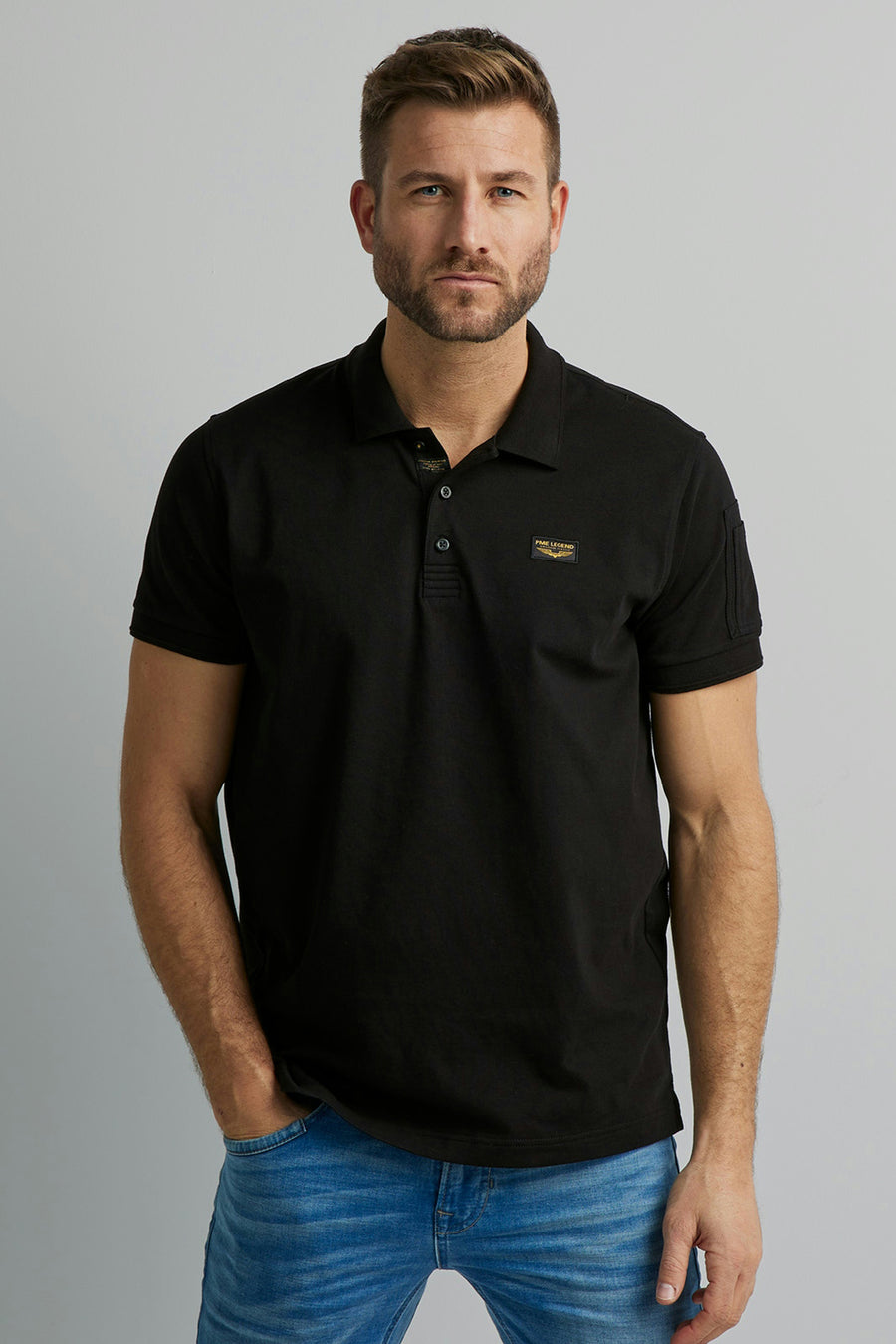 Polo noir de Pme Legend avec un écusson logo sur la poitrine, porté avec un jean bleu clair.