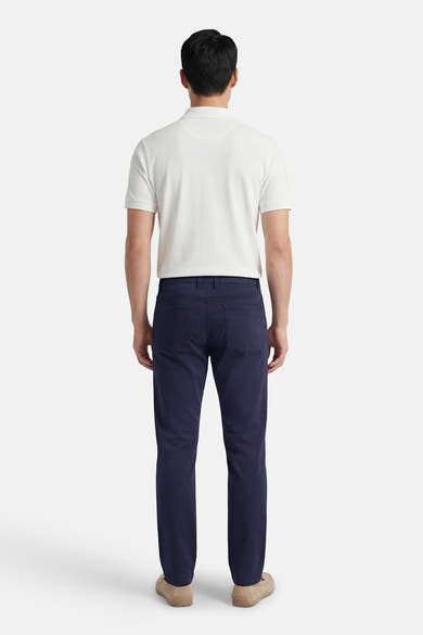 Gekleurde blauwe broek van PRIVATE BLUE, van achteren gezien, gedragen met een witte polo en lichtbruine loafers.