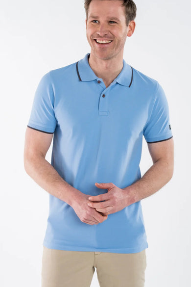 Polo bleu de PRESLY & SUN, avec bordure marron au col et aux manches, porté avec un pantalon beige.
