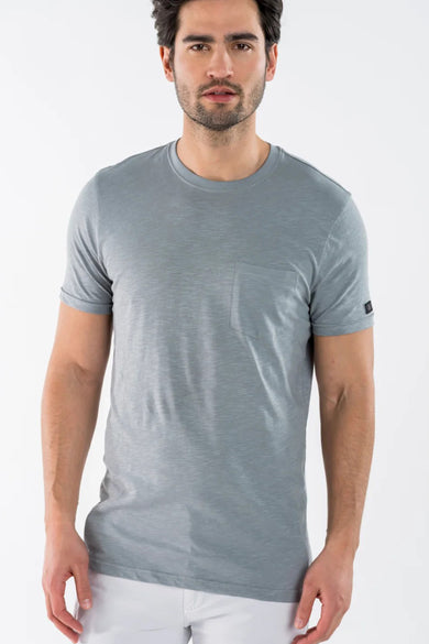 T-shirt bleu à manches courtes de PRESLY & SUN, avec poche poitrine, porté avec un pantalon blanc.