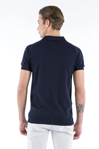 Polo bleu marine de PRESLY & SUN, manches courtes, porté avec un pantalon blanc, vue de dos.