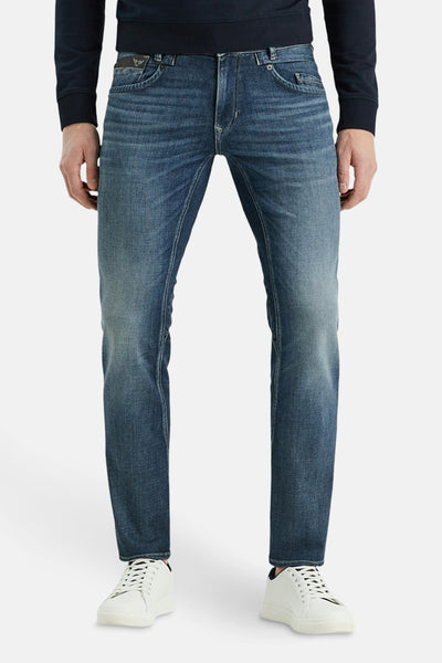 Jean tapered bleu de PME Legend, porté avec un pull bleu marine et des baskets blanches.