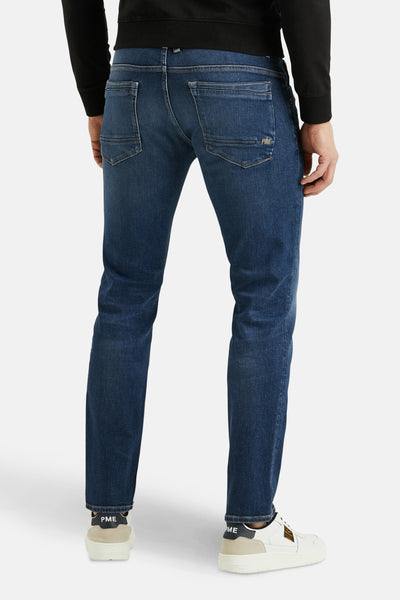 Jean droit bleu moyen de PME Legend, avec poches arrière et chaussures de sport blanches.