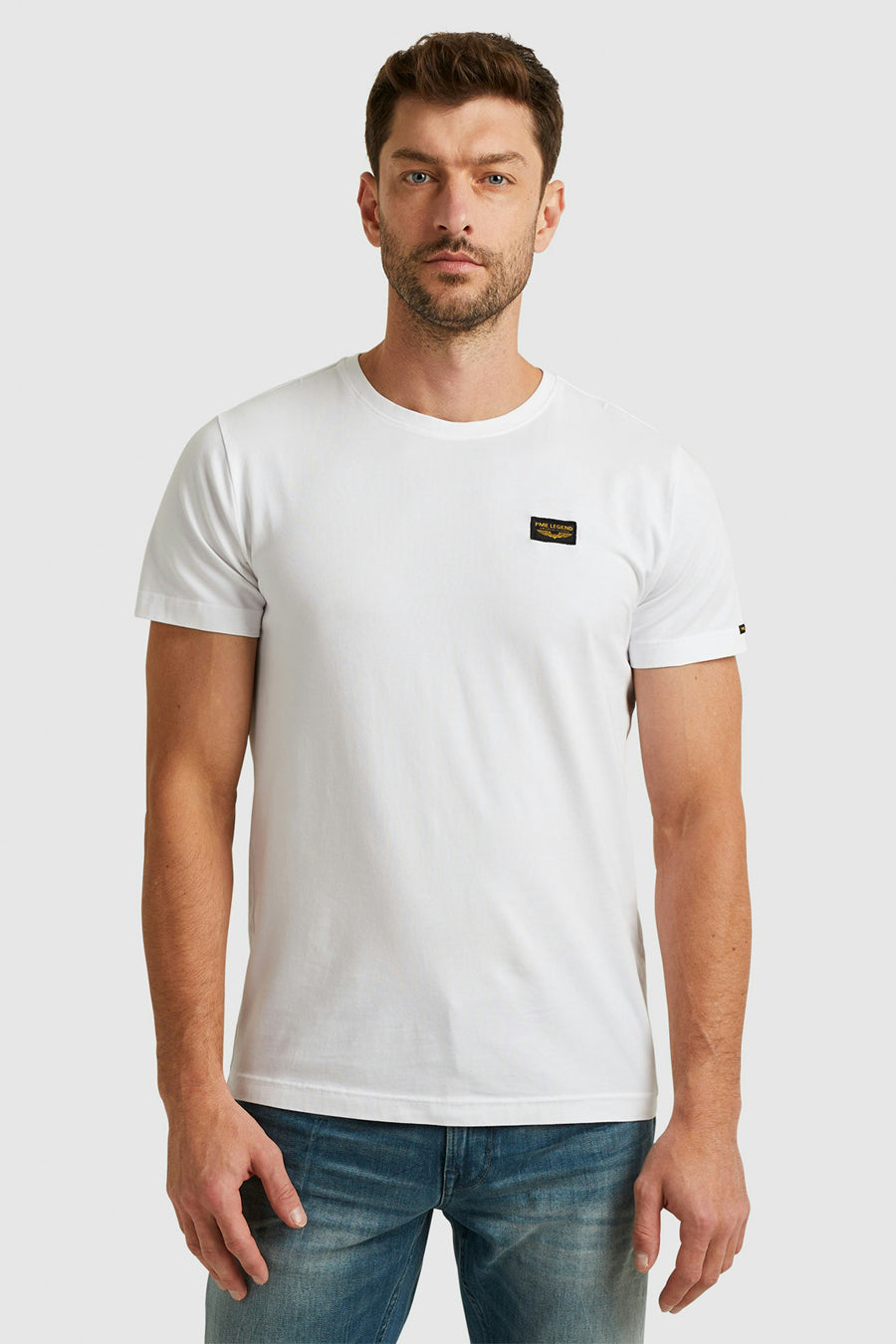 T-shirt blanc de Pme Legend avec un patch logo sur la poitrine, porté avec un jean bleu.
