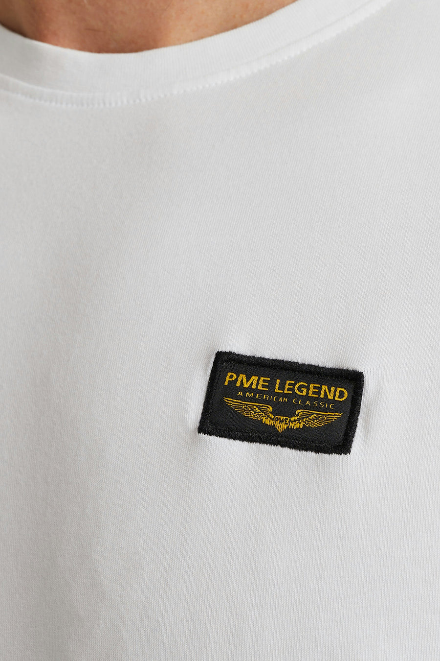 T-shirt blanc de Pme Legend, avec un patch logo noir et doré sur la poitrine.
