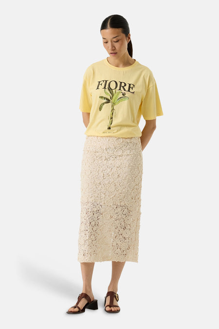 T-shirt jaune à manches courtes de GARCIA, imprimé d'une plante de banane et du mot FIORE, porté avec une jupe crayon en dentelle beige.