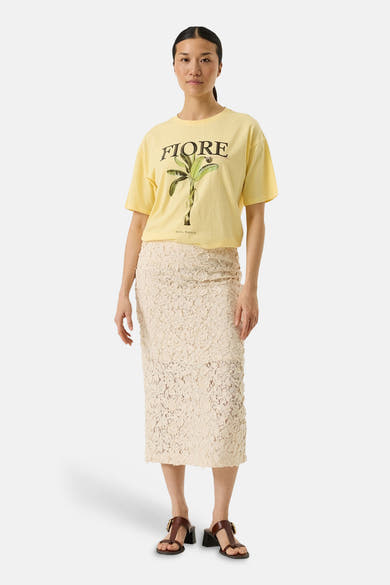 T-shirt jaune à manches courtes de GARCIA, avec imprimé 'FIORE' et bananier, porté avec une jupe en dentelle écrue.