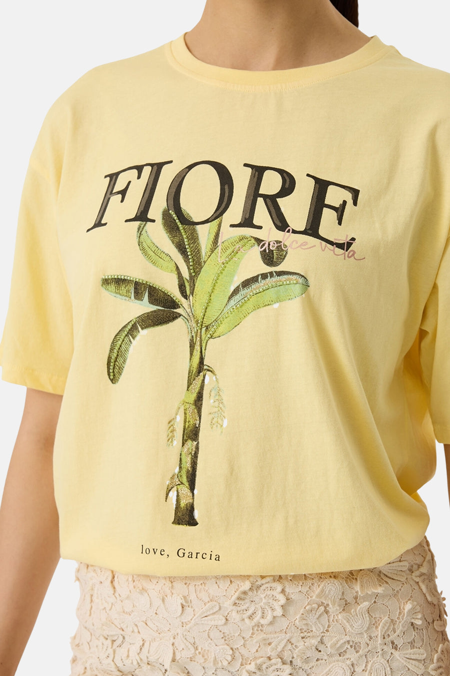 T-shirt jaune de GARCIA avec imprimé palmier banane, texte "FIORE" et "love, Garcia", porté avec une jupe en dentelle.