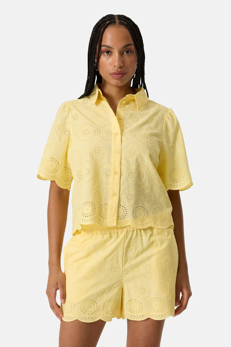 Chemise à manches courtes jaune de GARCIA en broderie anglaise avec col, manches bouffantes et ourlet festonné, portée avec un short assorti.