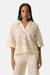Chemise à manches courtes beige de GARCIA en dentelle florale avec un col ouvert, portée avec un pantalon assorti.
