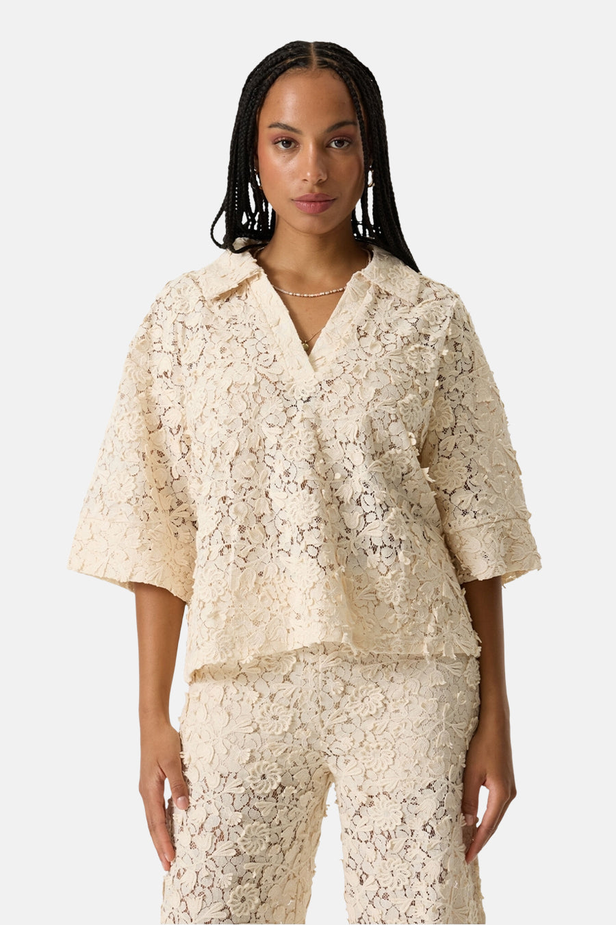 Chemise à manches courtes beige de GARCIA en dentelle florale avec un col ouvert, portée avec un pantalon assorti.