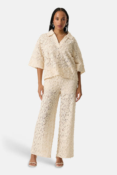 Chemise à manches courtes beige de GARCIA en dentelle florale texturée, avec col V, portée avec un pantalon assorti.