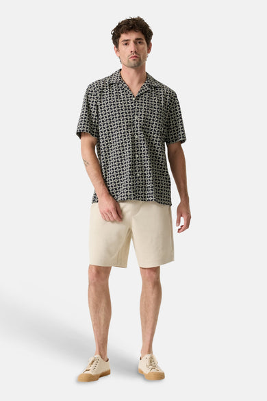 Multicolored short-sleeve shirt with geometric print, worn by model with beige shorts and white sneakers, front view