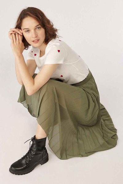 Olive green pleated 3/4 length skirt with flowing fabric, worn with white heart-print tee and black combat boots, lifestyle pose.