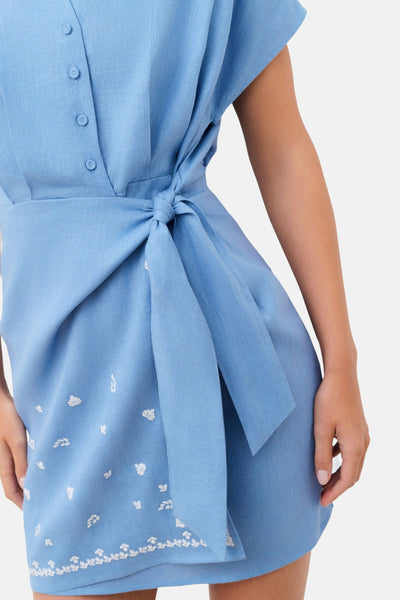 Robe bleu ciel en lin de CAROLL, boutonnée, avec une ceinture à nouer et des broderies florales blanches.