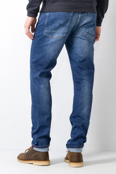 Jean tapered bleu moyen de Petrol Industries®, avec ourlets roulés et des chaussures marron.
