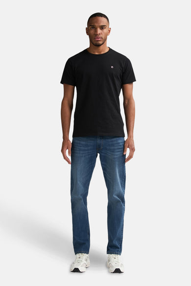 Jeans fuselés bleu moyen de Petrol Industries, portés avec un t-shirt noir et des baskets blanches.