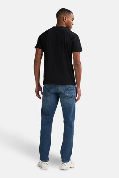 Jean fuselé bleu moyen de Petrol Industries, porté avec un t-shirt noir uni et des baskets blanches, vue de dos.
