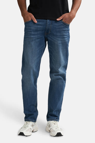 Jean fuselé bleu moyen de Petrol Industries®, porté avec un t-shirt noir et des chaussures de sport blanches.
