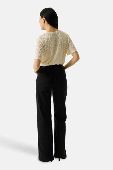 Ecru short-sleeve textured top with wavy pattern, back view, paired with black wide-leg pants