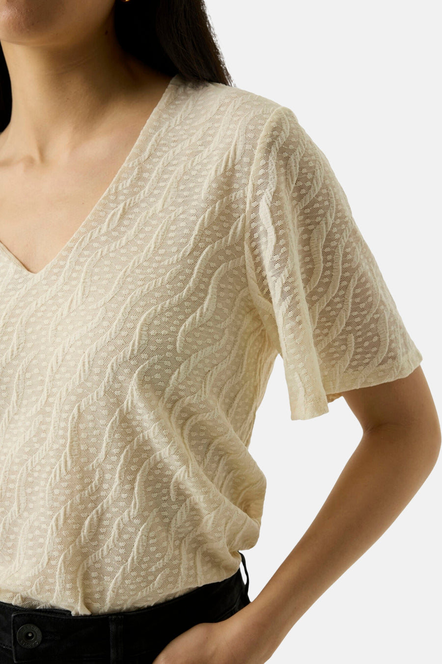 Ecru short-sleeve textured knit top with V-neck and wavy cable pattern, worn with black pants, side view