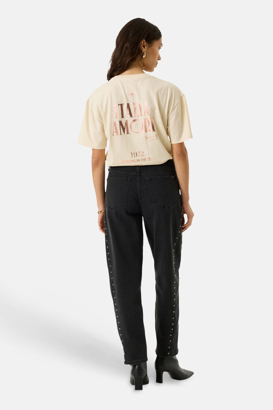 Ecru short-sleeve T-shirt with "ITALIA AMORI" graphic back print, worn with black studded jeans and boots, back view.