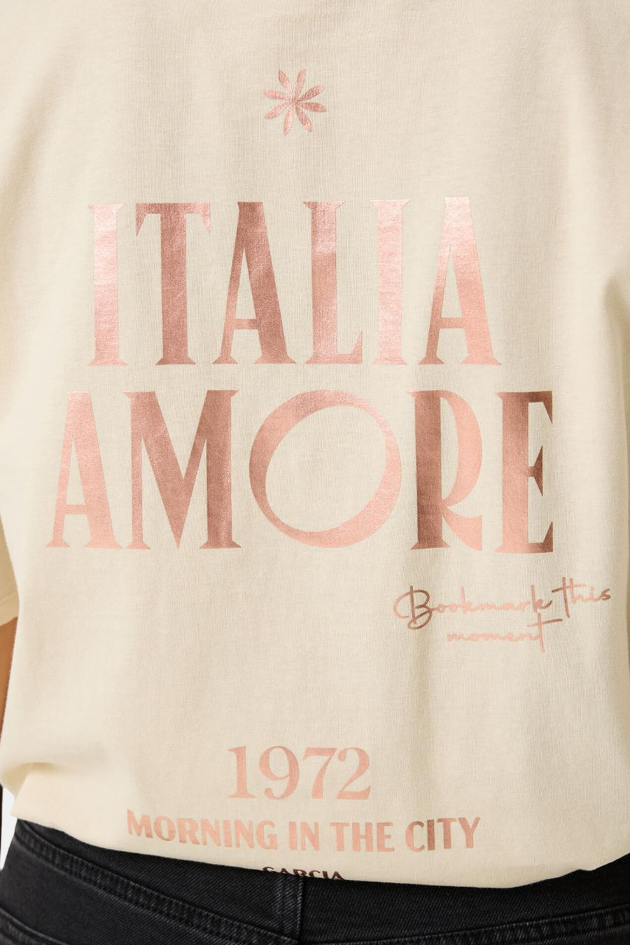 Ecru short-sleeve t-shirt with rose gold "ITALIA AMORE" print, floral accent, and "1972 Morning in the City" text, worn with black jeans, front cropped view