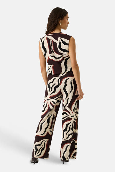 Multicolored wide-leg elastic waist trousers with abstract black, cream, and burgundy pattern, back view on model wearing sleeveless top and black heels