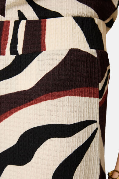 Multicolored elastic waist women's seasonal pants with abstract black, red, and cream pattern, textured ribbed fabric, side view close-up