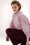 Pink striped long-sleeve blouse with relaxed fit and contrast panel, worn by model in side view with burgundy pants.