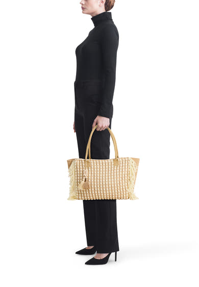 Sac à bandoulière beige de Access® avec motifs ovales en relief et franges, tenu par une femme.