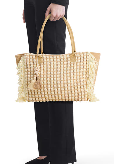 Sac à bandoulière beige de Access®, à motif de pois crème, franges et breloques à pompons, porté par une personne.
