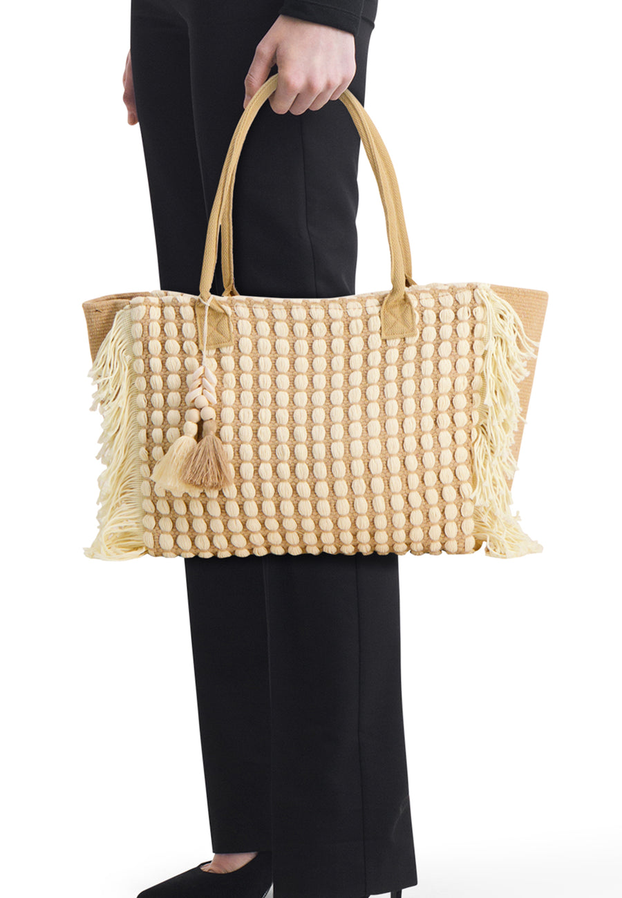 Sac à bandoulière beige de Access®, à motif de pois crème, franges et breloques à pompons, porté par une personne.