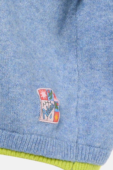 Pull à col rond bleu d'ADORE avec un écusson décoratif sur la poitrine et des finitions côtelées.
