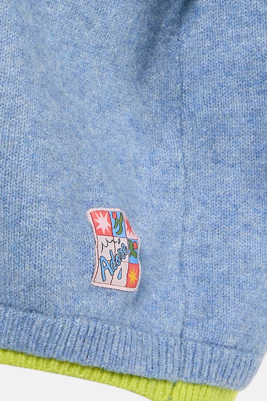 Pull à col rond bleu d'ADORE avec un écusson décoratif sur la poitrine et des finitions côtelées.
