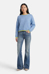 Pull à col rond bleu de ADORE avec bordure contrastée au col et aux poignets, porté avec un jean évasé et des escarpins.