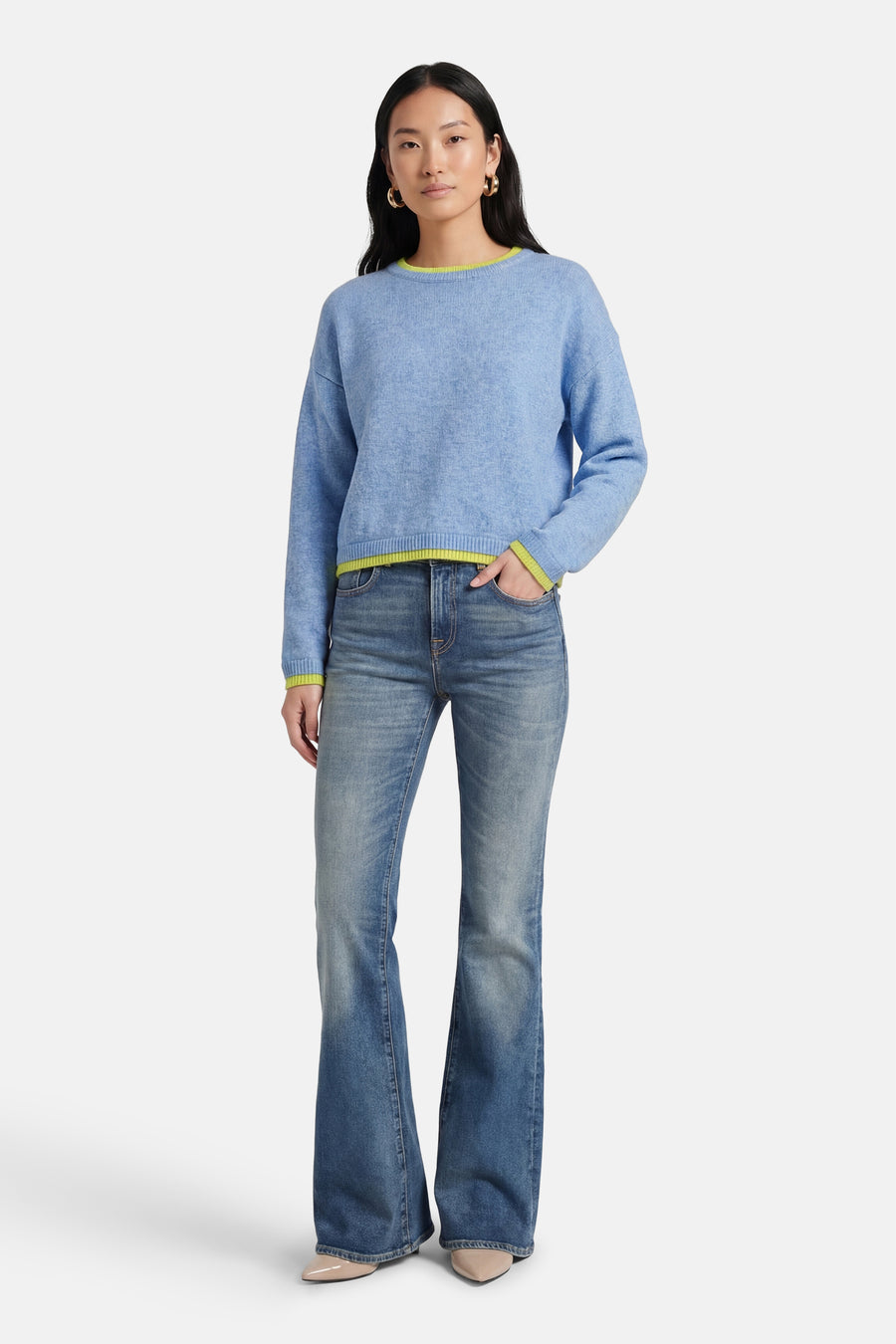 Pull à col rond bleu de ADORE avec bordure contrastée au col et aux poignets, porté avec un jean évasé et des escarpins.