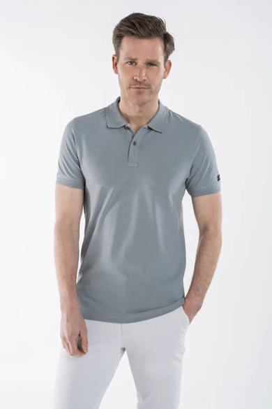 Polo gris de PRESLY & SUN, porté avec un pantalon blanc, main dans la poche.