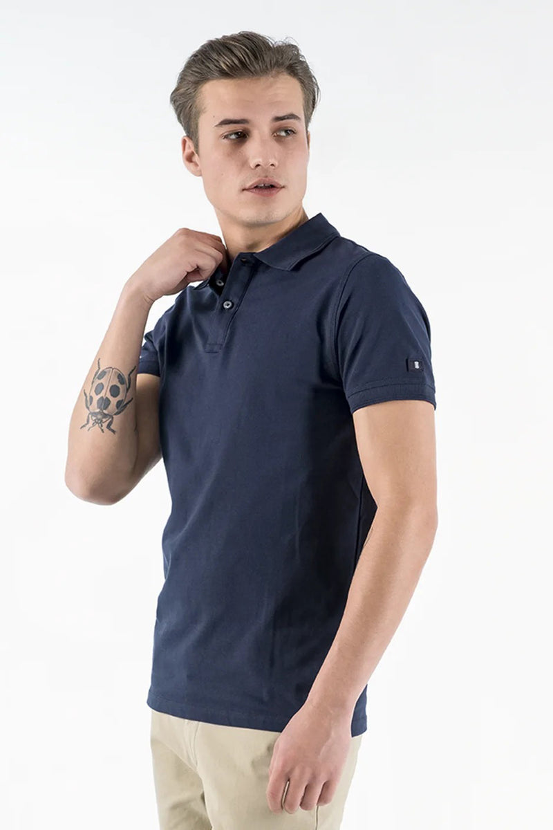 Polo bleu de PRESLY & SUN, porté avec un pantalon chino beige, vue de côté, tatouage sur le bras.

