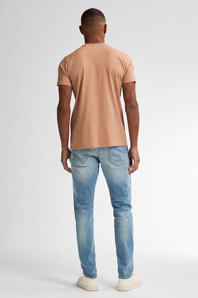 Slim jeans van Petrol Industries in lichtblauw gewassen denim, gedragen met een effen perzikkleurig T-shirt en crèmekleurige sneakers.