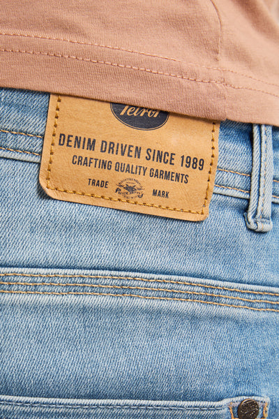 Jean slim en denim bleu clair de Petrol Industries, détail de l'étiquette en cuir à la taille et surpiqûres camel.
