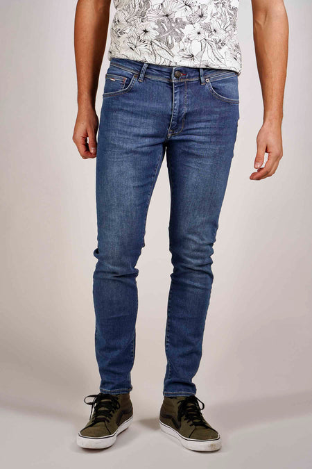 Blauwe slim fit jeans van Petrol Industries, gedragen met een T-shirt met bloemenprint en kaki hoge sneakers.