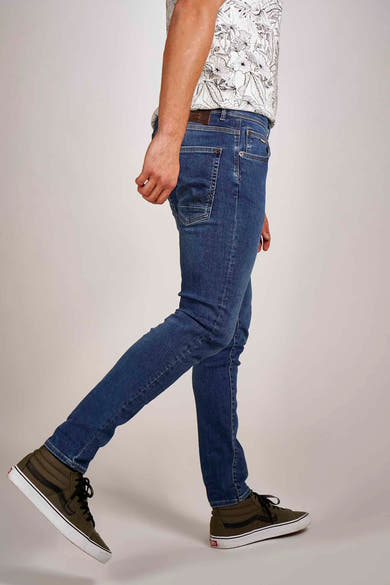 Blauwe slim fit jeans van Petrol Industries®, gedragen met een T-shirt met bloemenprint en hoge sneakers.