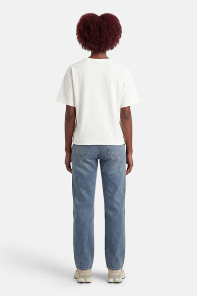 T-shirt à manches courtes blanc par ADORE, porté avec un jean bleu et des baskets beiges, vue de dos.
