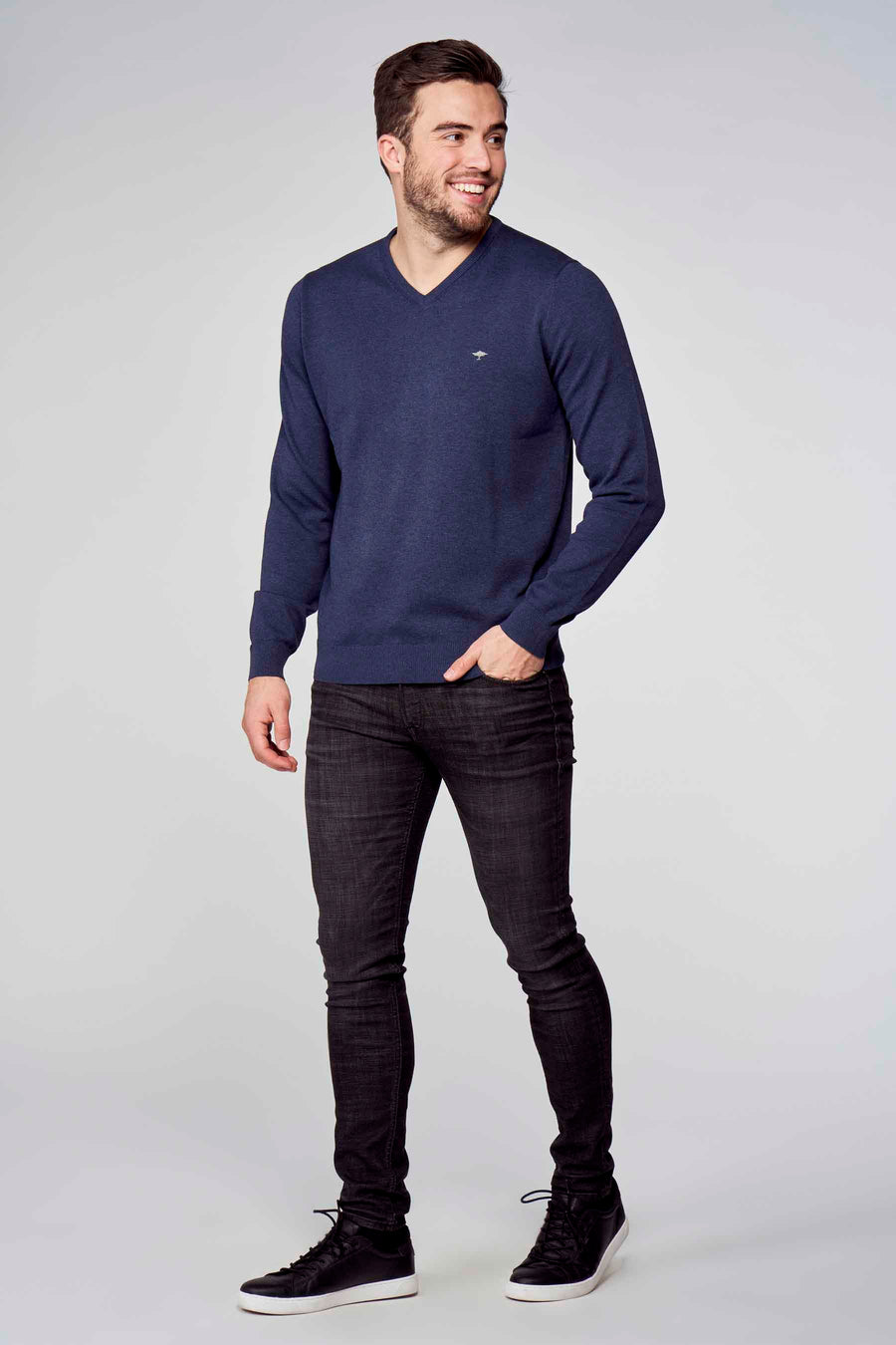 Pull col V bleu de Fynch-Hatton, porté avec un jean noir et des baskets noires à semelle blanche.
