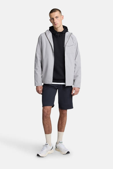 Short bleu de LYLE & SCOTT, porté avec un sweat à capuche noir, une veste grise et des baskets blanches.