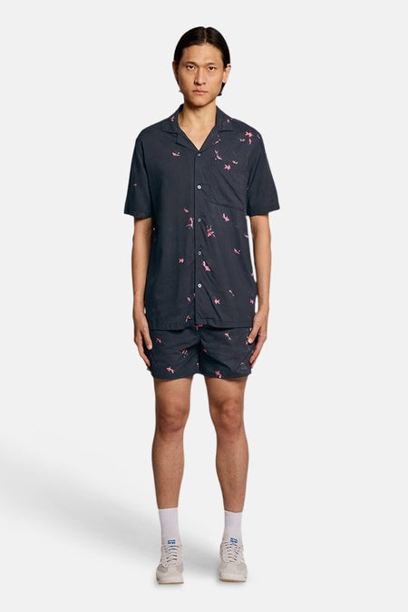 Short de bain bleu foncé à motifs d'oiseaux roses de LYLE & SCOTT, porté avec une chemise assortie.
