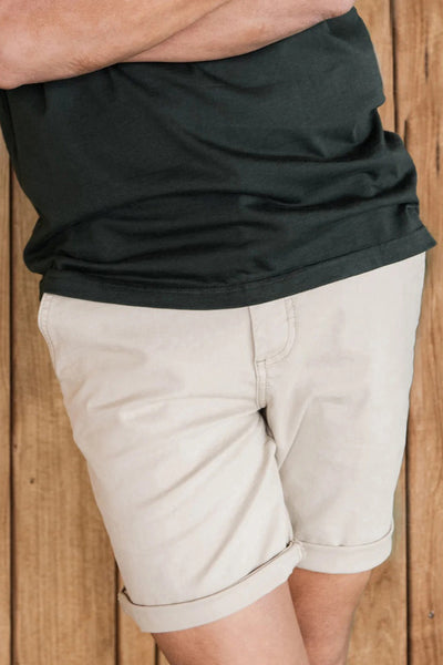 Short beige de PRESLY & SUN, avec ourlets roulés, porté avec un t-shirt vert foncé.